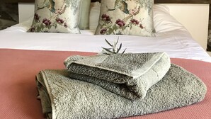 A neatly made bed with floral pillows, a folded blanket, and a welcome sign on a stone wall. - Casa da Oliveira (Pedrógão Grande)