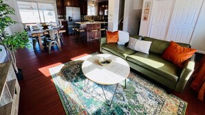 A spacious living area with a green sofa, a coffee table, and a dining table with chairs. There is a kitchen area with a refrigerator and a sink. - 15 min drive to Mile High! Sleeps 12! (Arvada)