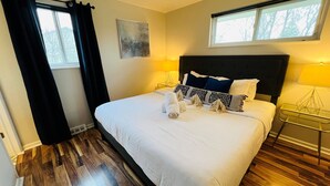 A neatly made bed with white linens and a black headboard, a bedside table with a lamp, and a window with curtains. - 15 min drive to Mile High! Sleeps 12! (Arvada)