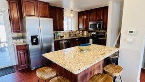 A modern kitchen with wooden cabinets, stainless steel appliances, a granite countertop, and wooden stools. - 15 min drive to Mile High! Sleeps 12! (Arvada)