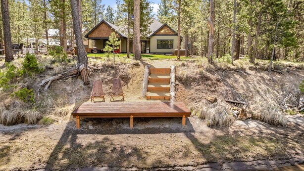 Une terrasse en bois avec des chaises, un petit escalier et une maison située dans une zone boisée.