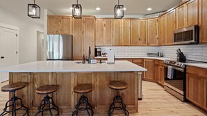 Une cuisine moderne avec des meubles en bois, un grand îlot central doté de tabourets, des appareils en acier inoxydable et un éclairage suspendu.