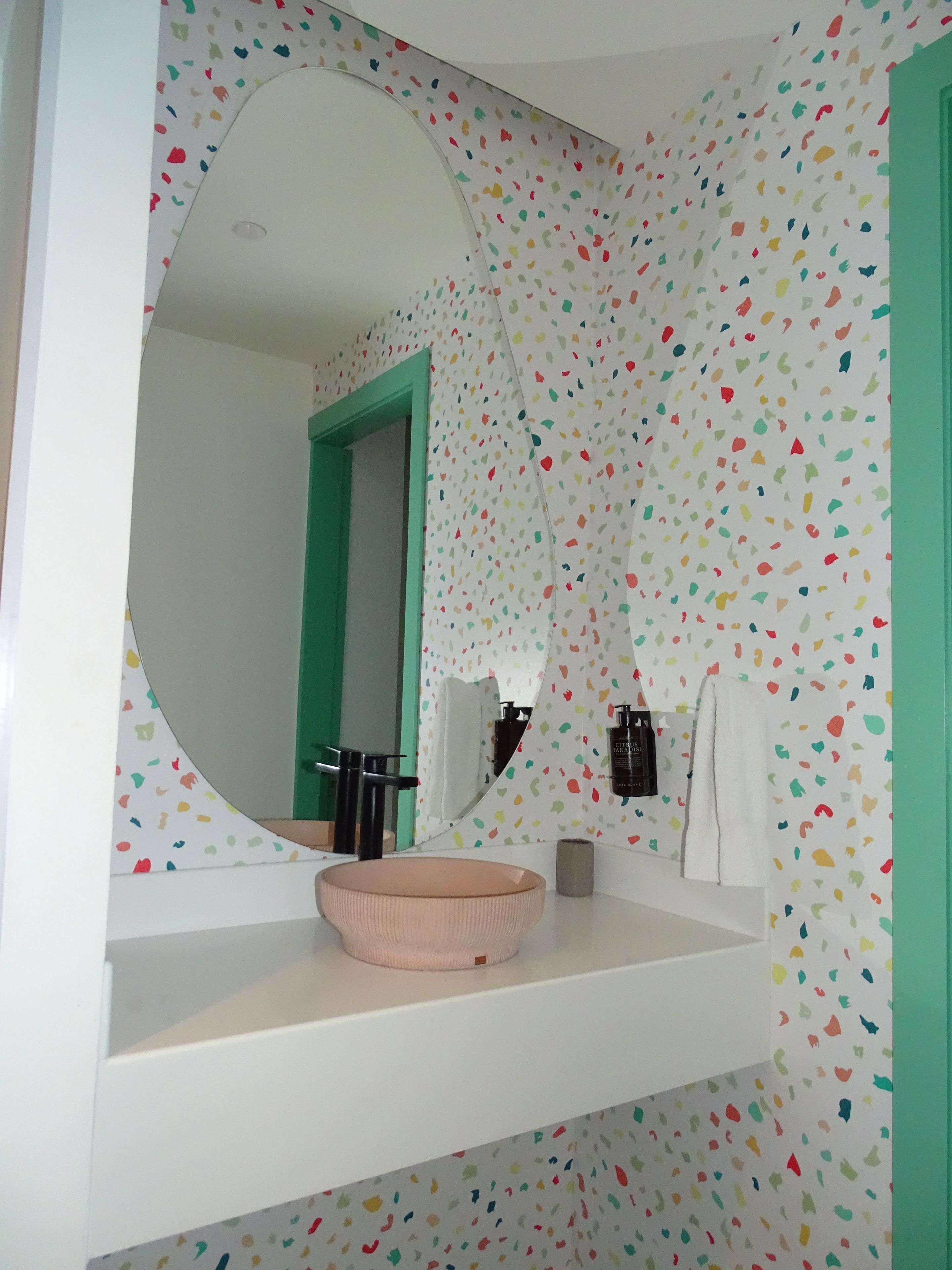 A bathroom with a round mirror, a pink sink, and a green door.