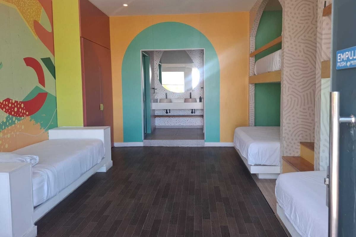 Una habitación de hotel con literas, una kitchenette pequeña y un mural colorido en la pared.