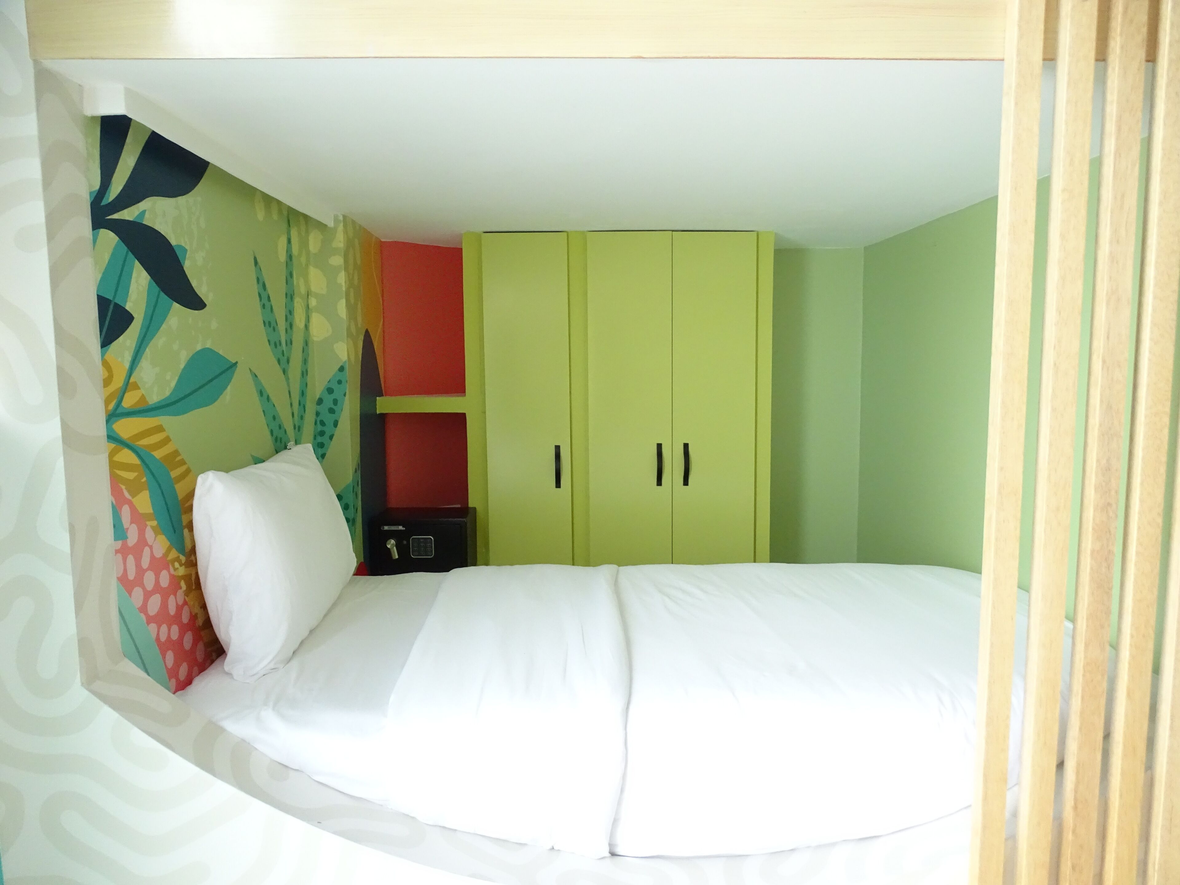 Una habitación con una cama, un armario verde, un aparador rojo y un papel tapiz estampado.