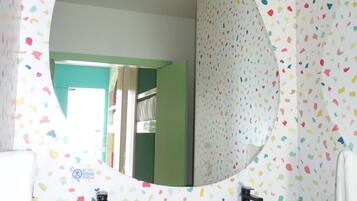 Un baño con un espejo redondo, dos lavamanos y una pared con un estampado de hojas de colores.