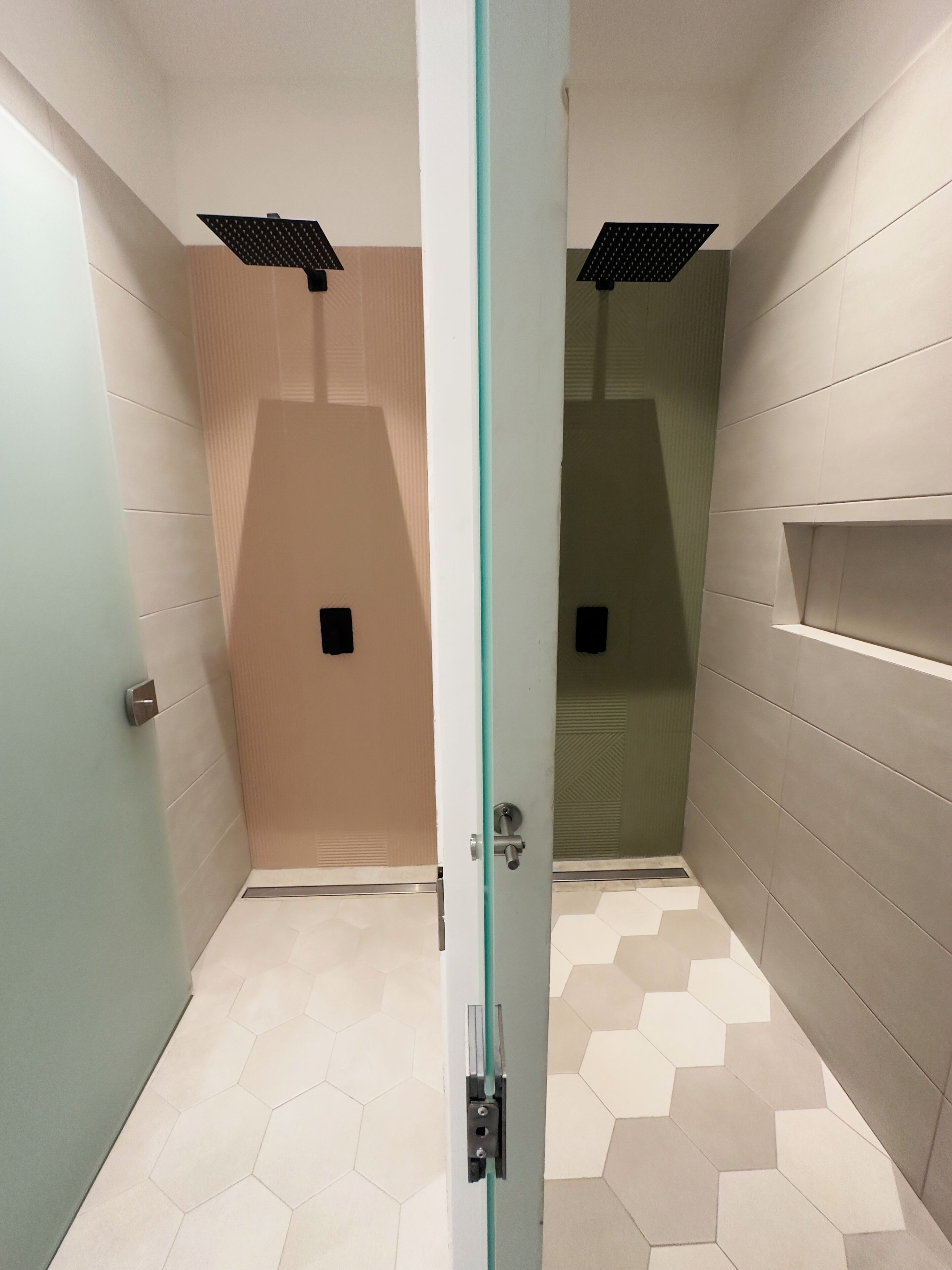 Un baño con puerta de cristal, baldosas hexagonales en el suelo e iluminación empotrada.