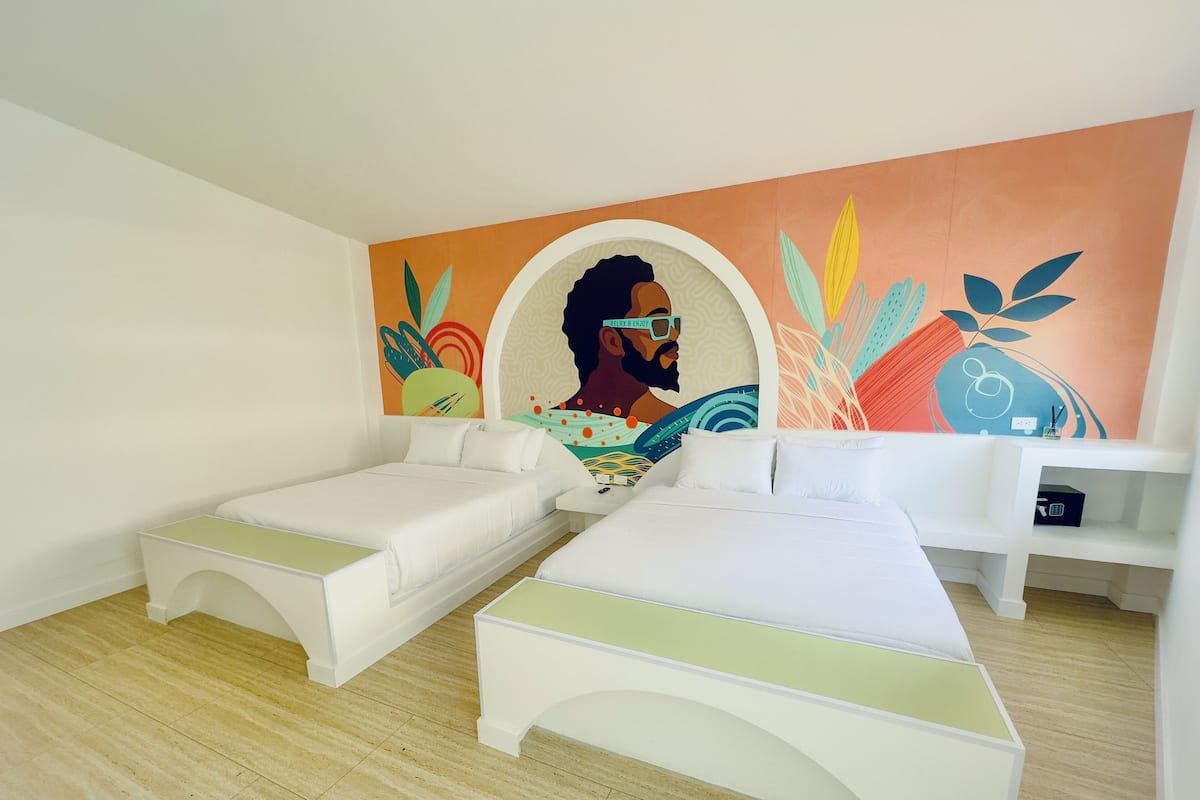 Una habitación con dos camas individuales, una mesa blanca y un mural colorido en la pared.