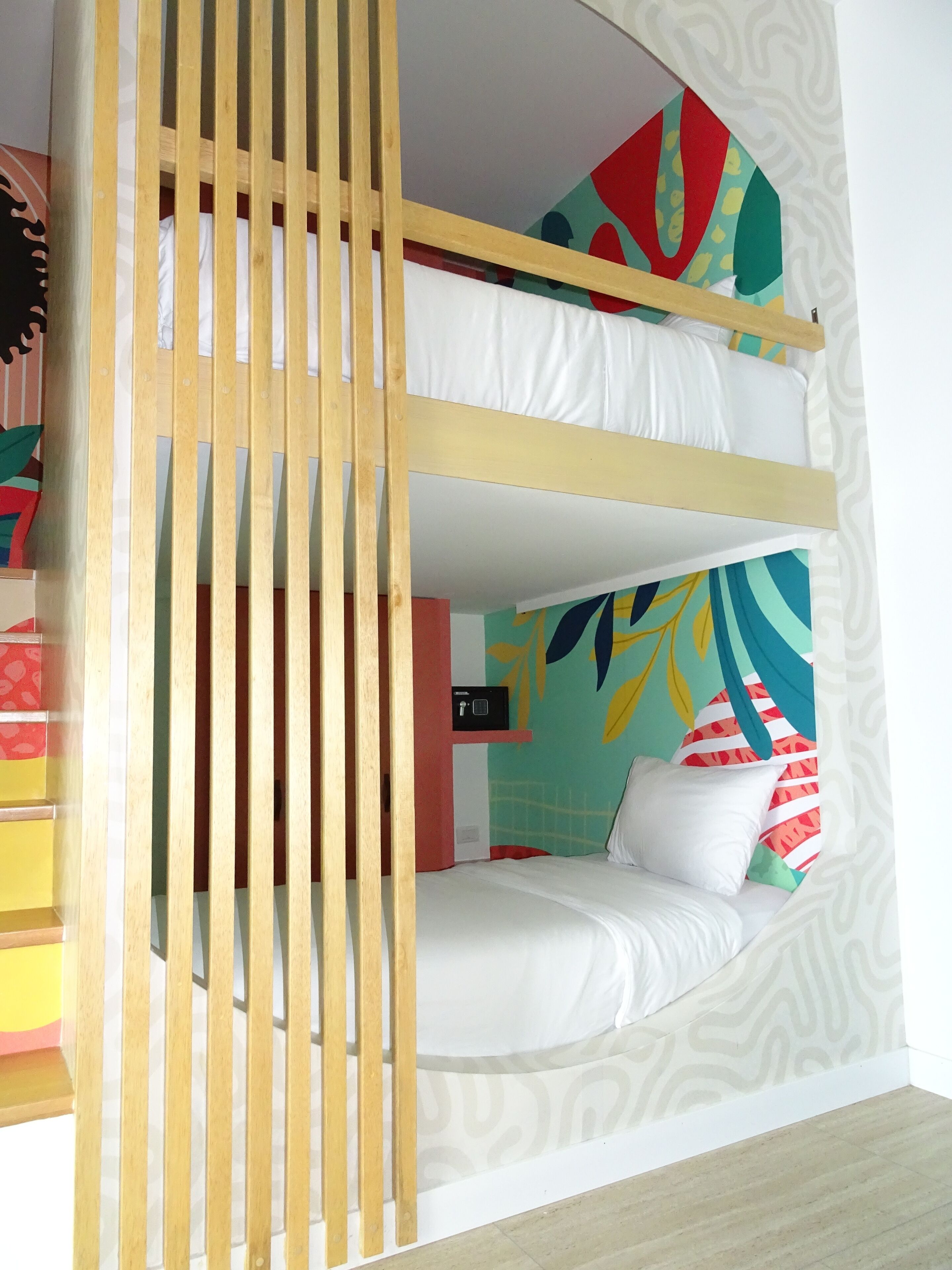 Een stapelbed met houten frame, een kleurrijke muurschildering en een klein kluisje.