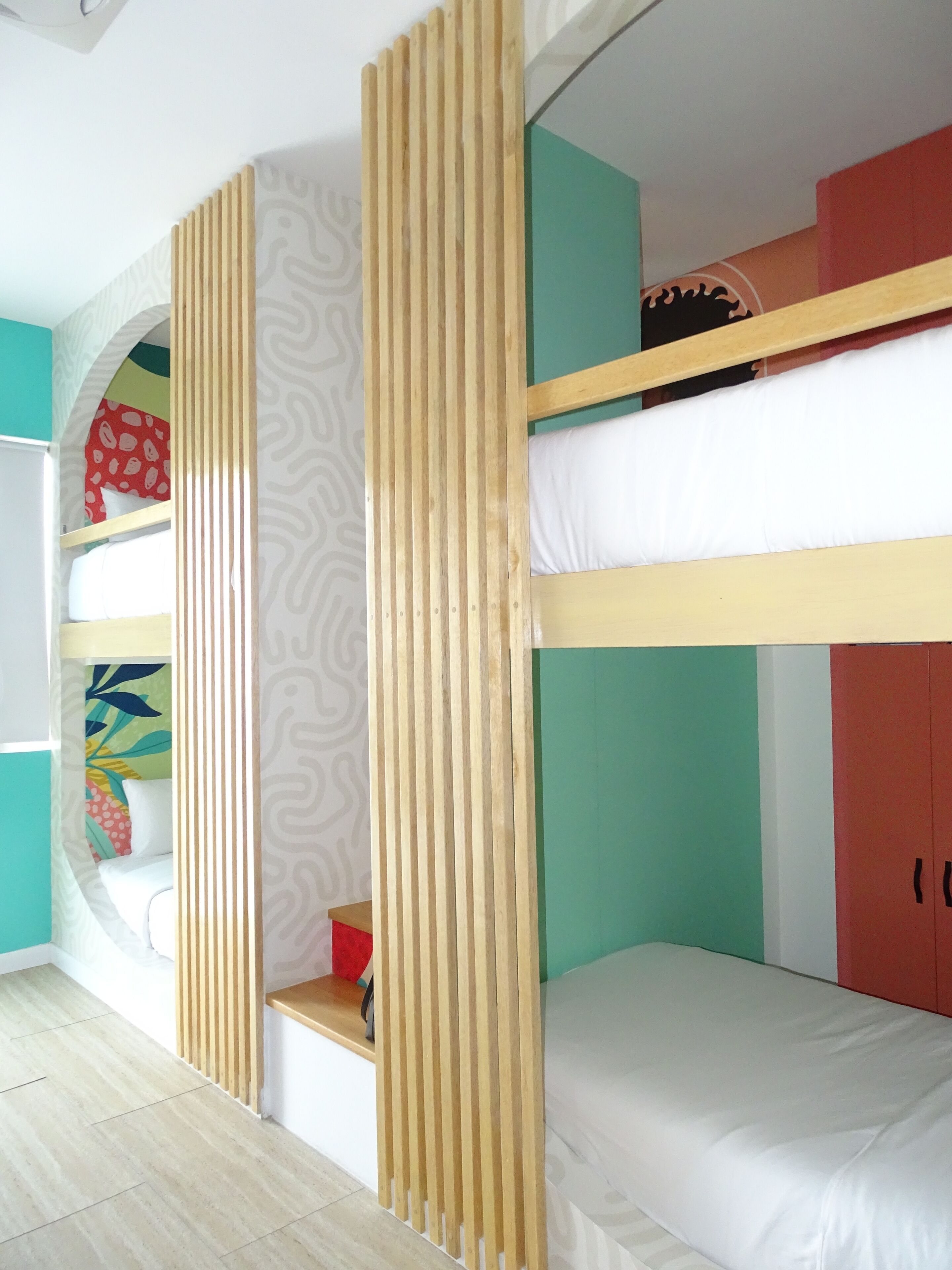 A bunk bed room with a wooden divider, a small shelf, and a colorful wall design.