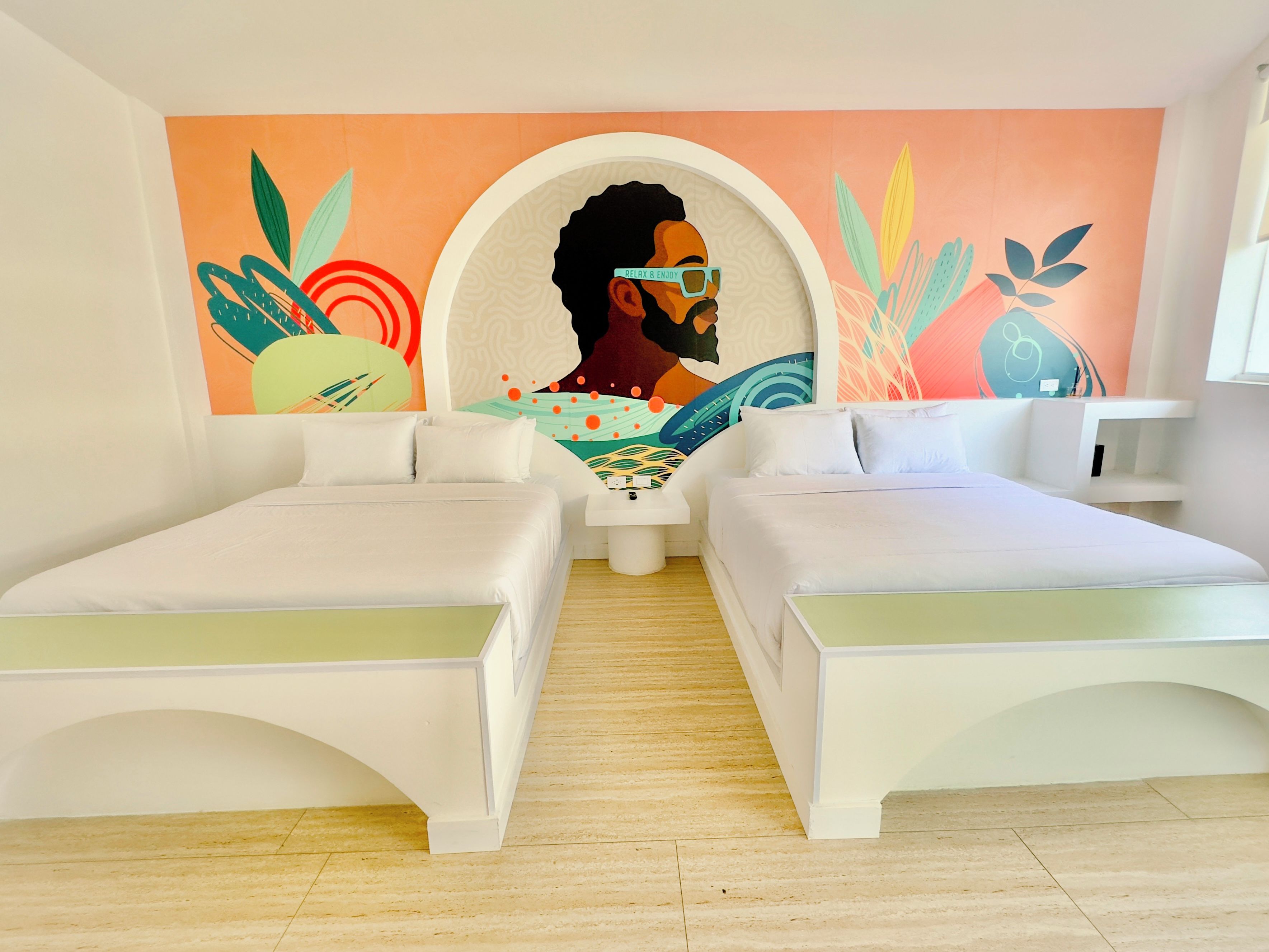 A hotel room with two beds, a mural on the wall, and a small table.