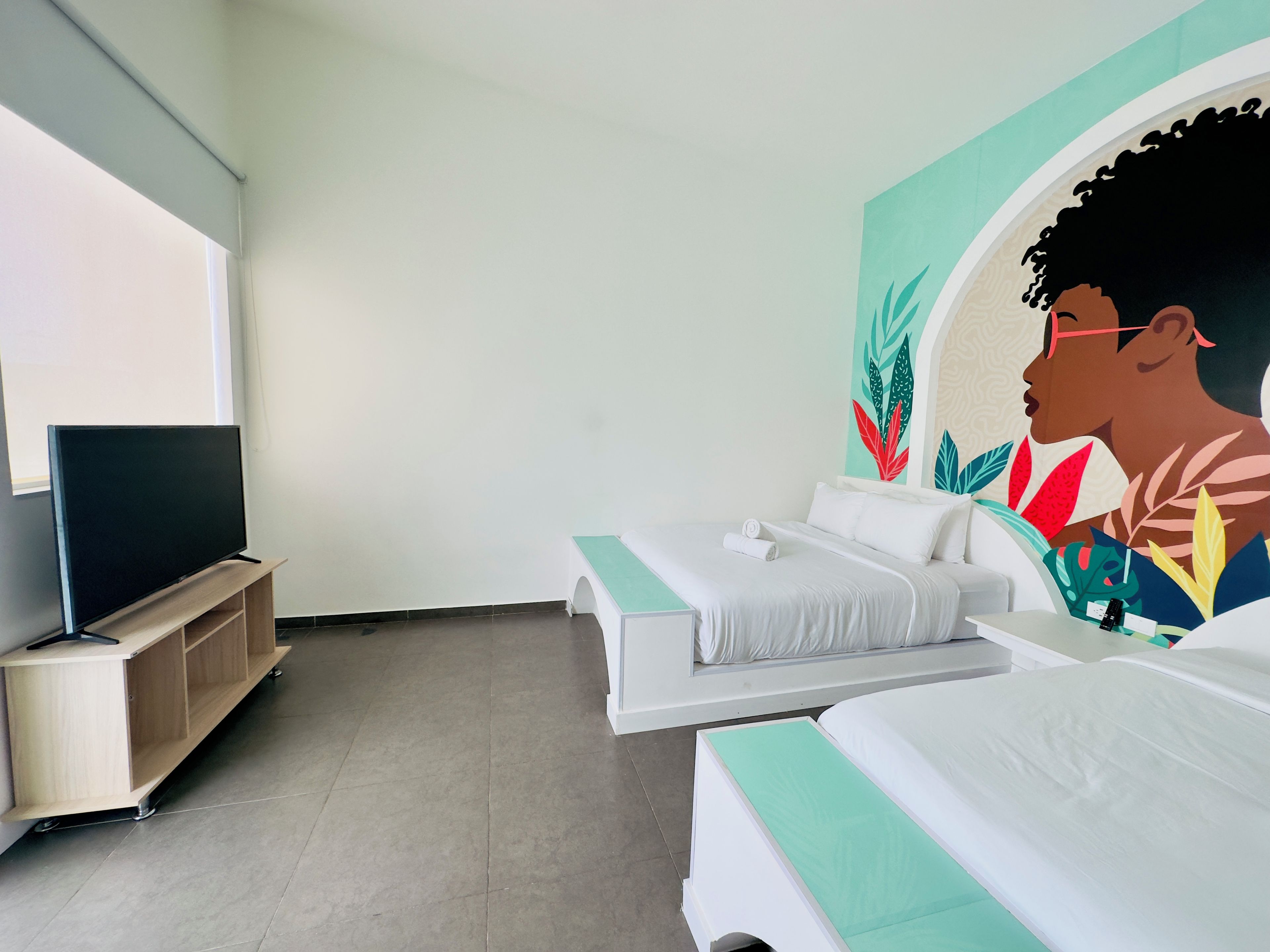 A hotel room with a bed, a TV, and a mural on the wall.