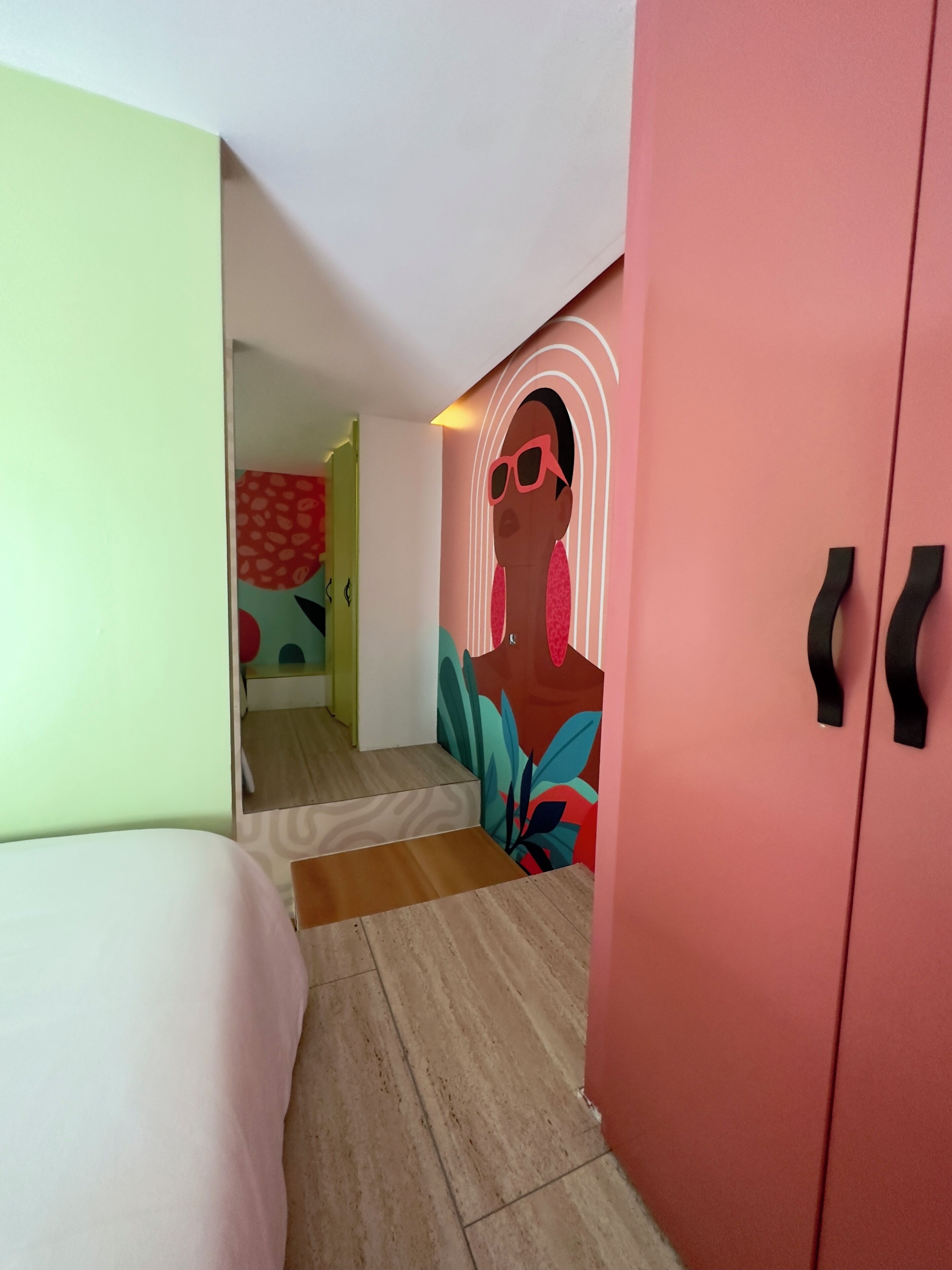 Una habitación de hotel moderna con una cama, un armario y un mural colorido en la pared.