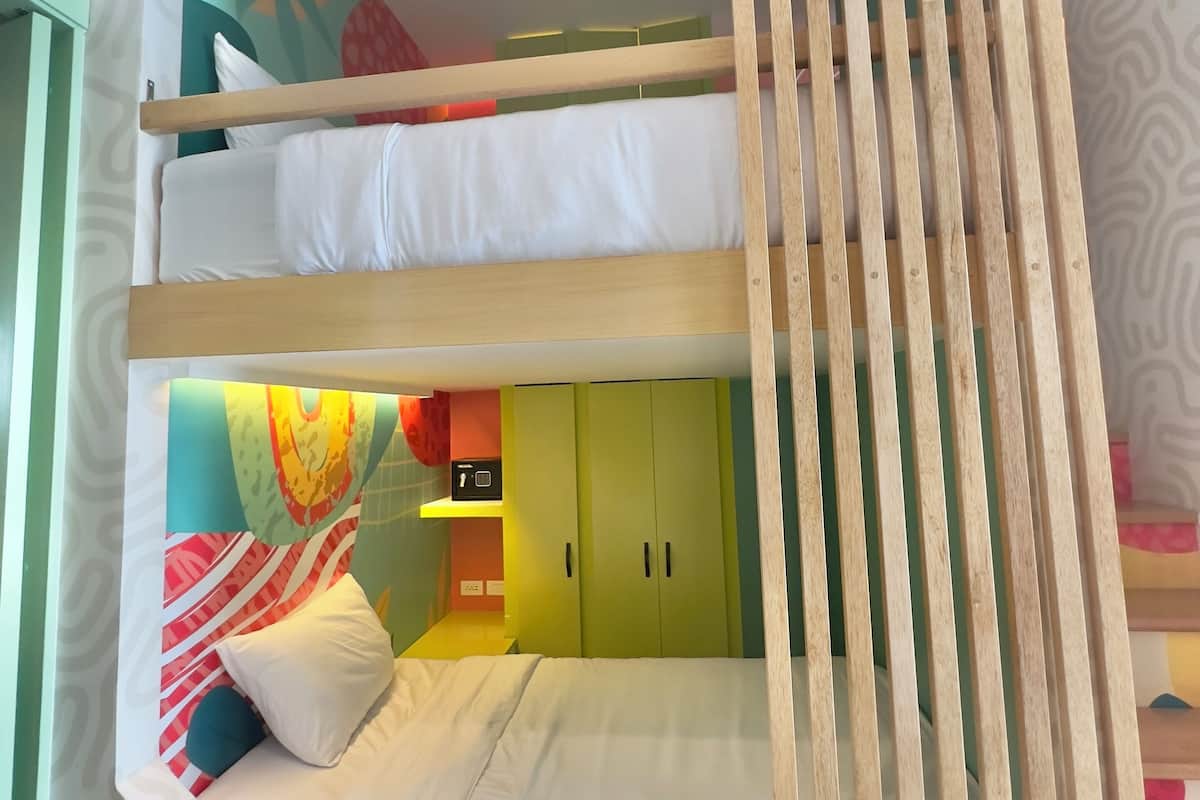 Habitación con literas, un diseño de pared curva, un armario verde y una estantería pequeña con un radio.