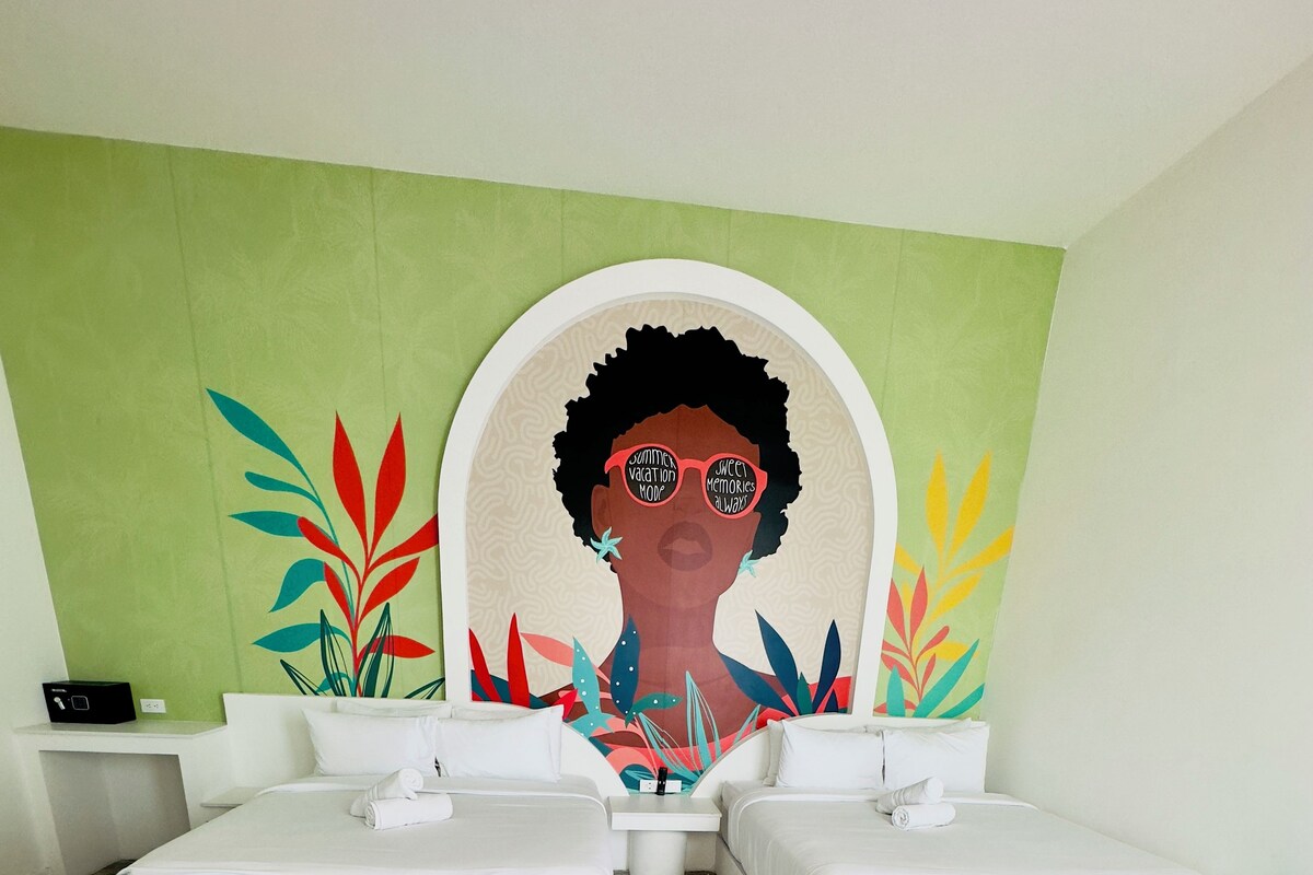 A hotel room with two beds, a green wall, and a large mural.