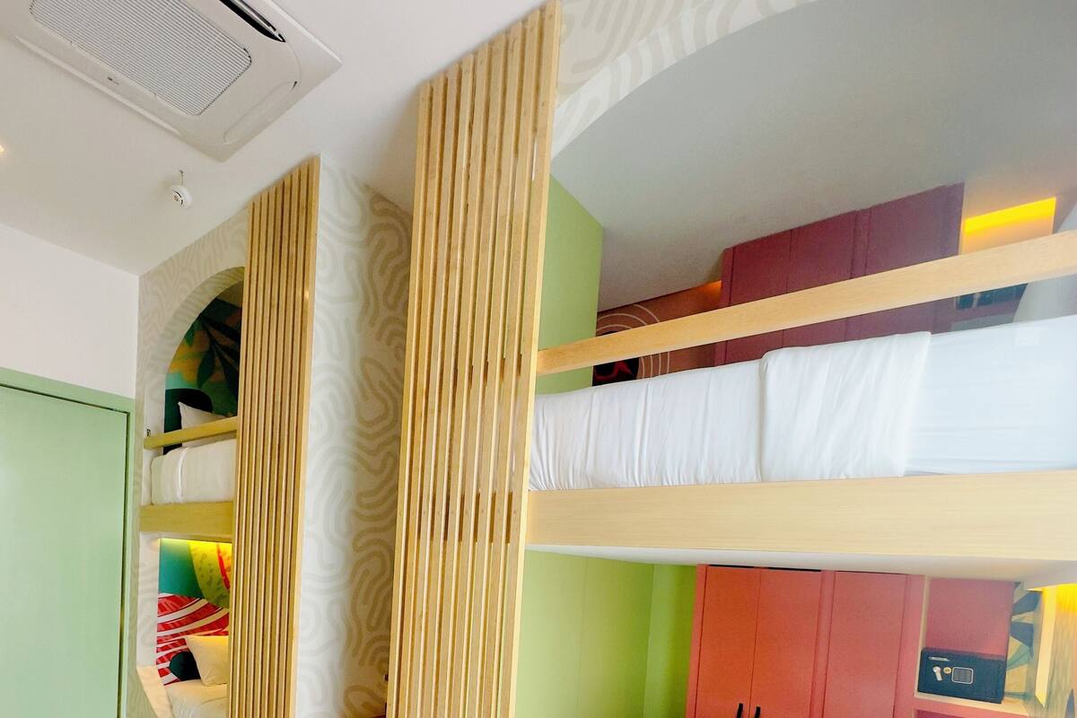 Habitación con literas, separador de madera, pared verde y un armario rojo.