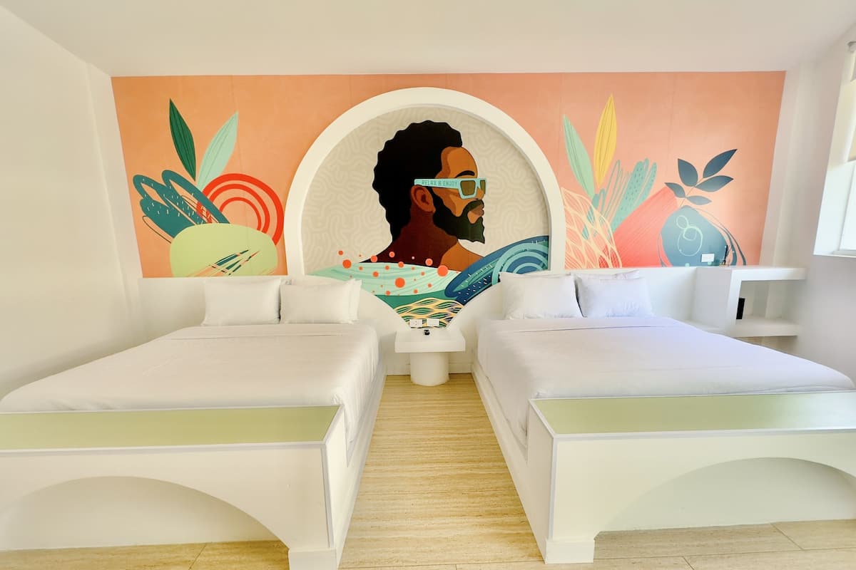 Una habitación de hotel moderna con dos camas blancas, un mural en la pared y una pequeña mesa blanca.