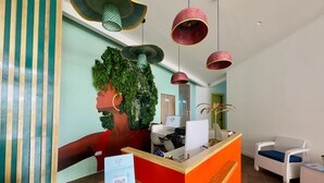 Un área de recepción con un escritorio de madera, una pared de acento roja y una gran obra de arte verde en la pared.