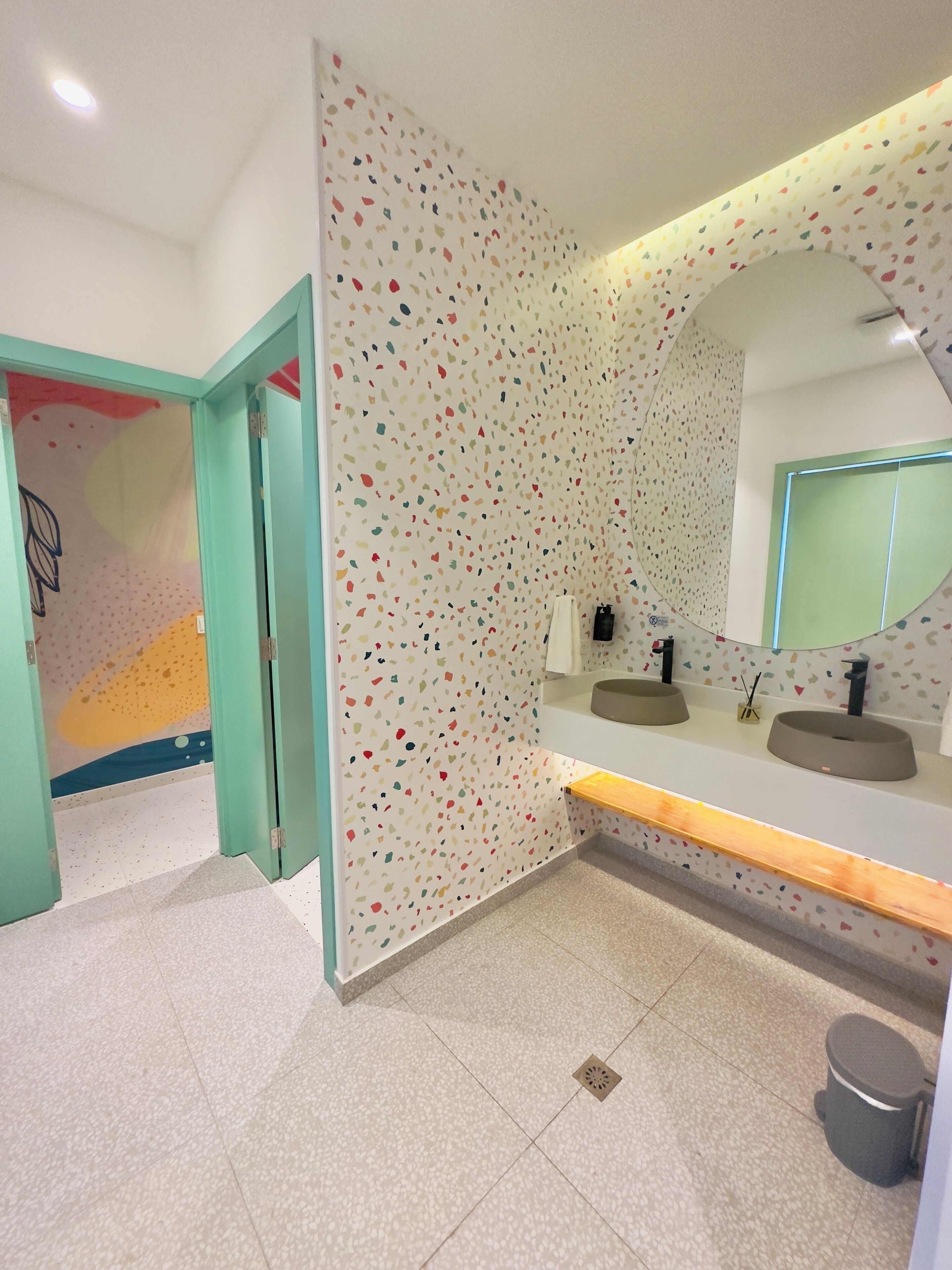 Un baño moderno con pared de azulejos moteados, un espejo grande y un mueble de tocador con dos lavamanos.