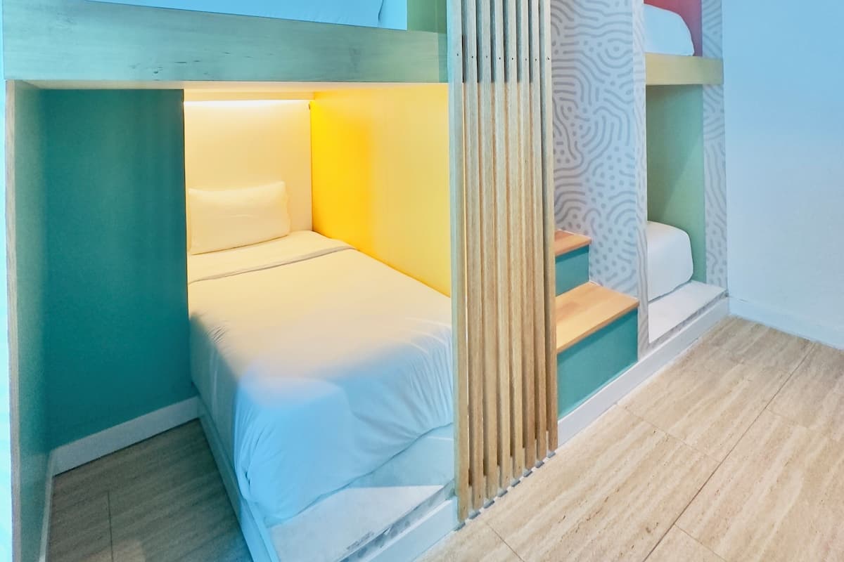 Habitación con literas, un separador de tela estampado, un pequeño rincón de descanso y una escalera.