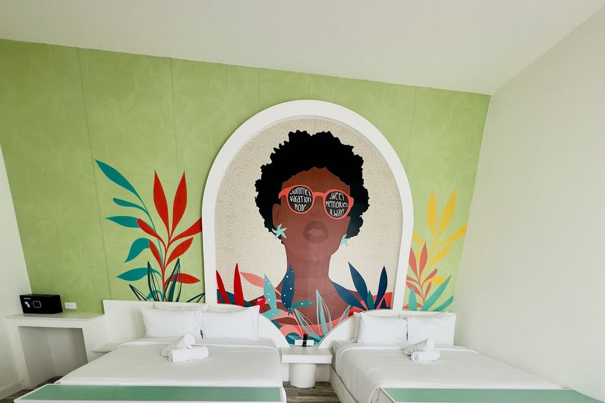Una habitación de hotel con dos camas, una pared verde y un mural grande.
