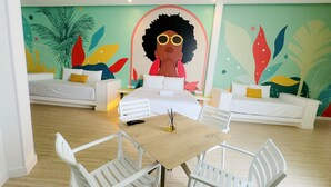 Una habitación de hotel moderna con un gran mural, dos sofás blancos, una mesa de madera y sillas blancas.