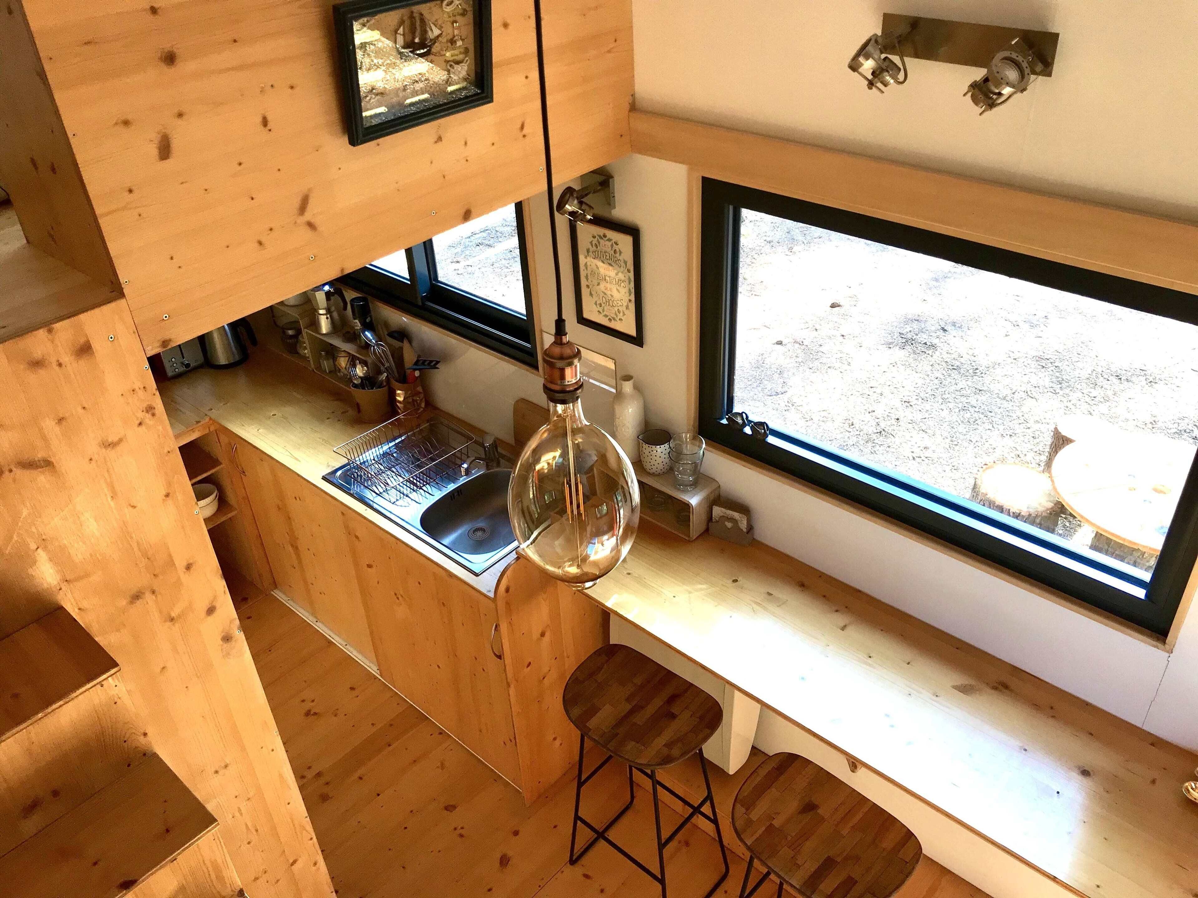 A compact kitchen with wooden cabinetry, a stainless steel sink, and a hanging light fixture.
