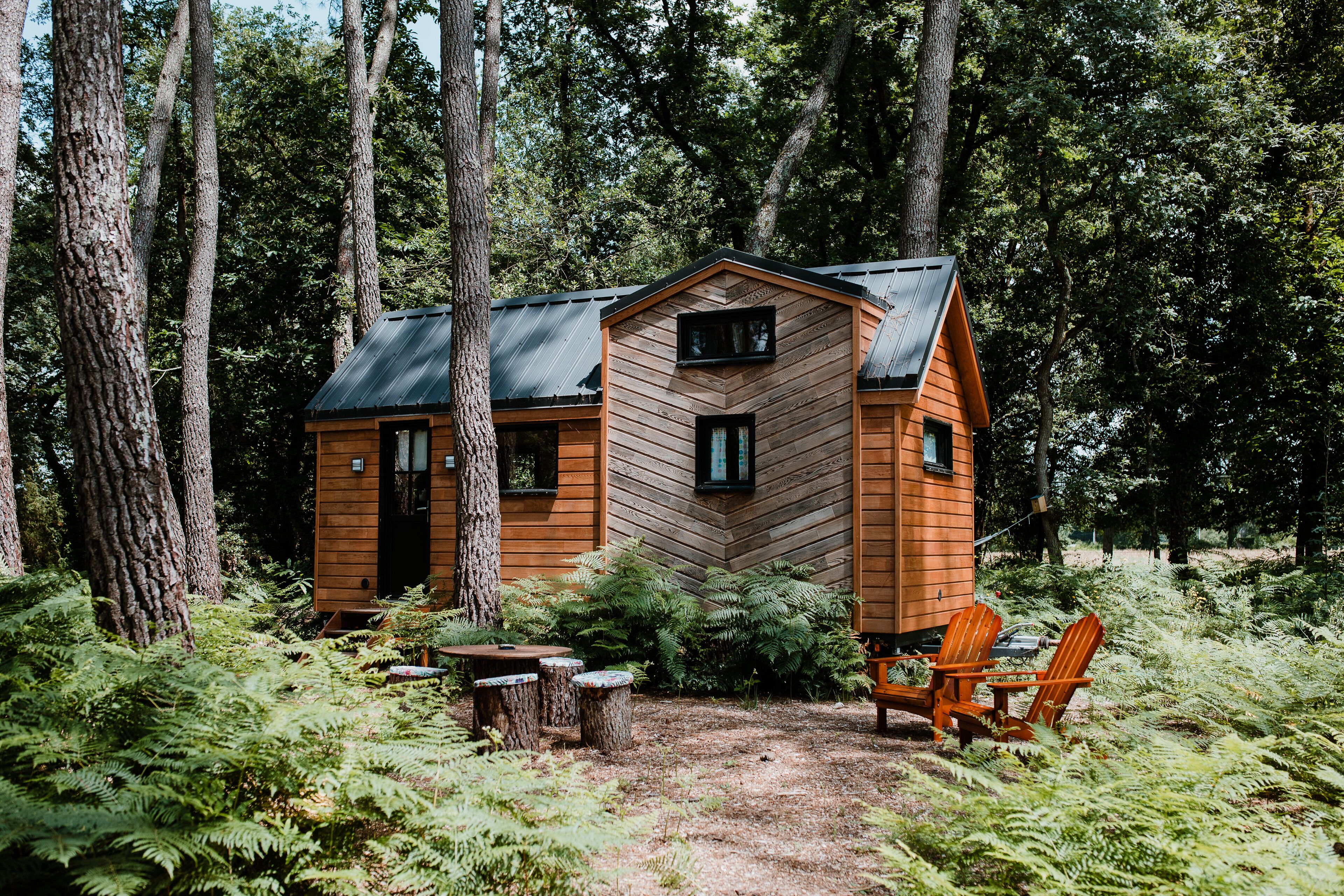 A cabin with a hipped roof, wooden exterior, and a small porch with Adirondack chairs.