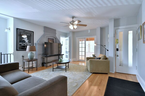 A modern living room with a fireplace, a ceiling fan, and a large window.