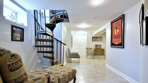 Un vaste espace de vie agrémenté d’un canapé à motifs, d’un escalier et d’une affiche sportive encadrée au mur.