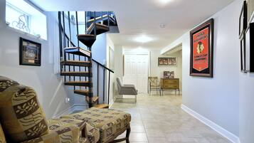 A spacious living area with a patterned sofa, a staircase, and a framed sports poster on the wall.