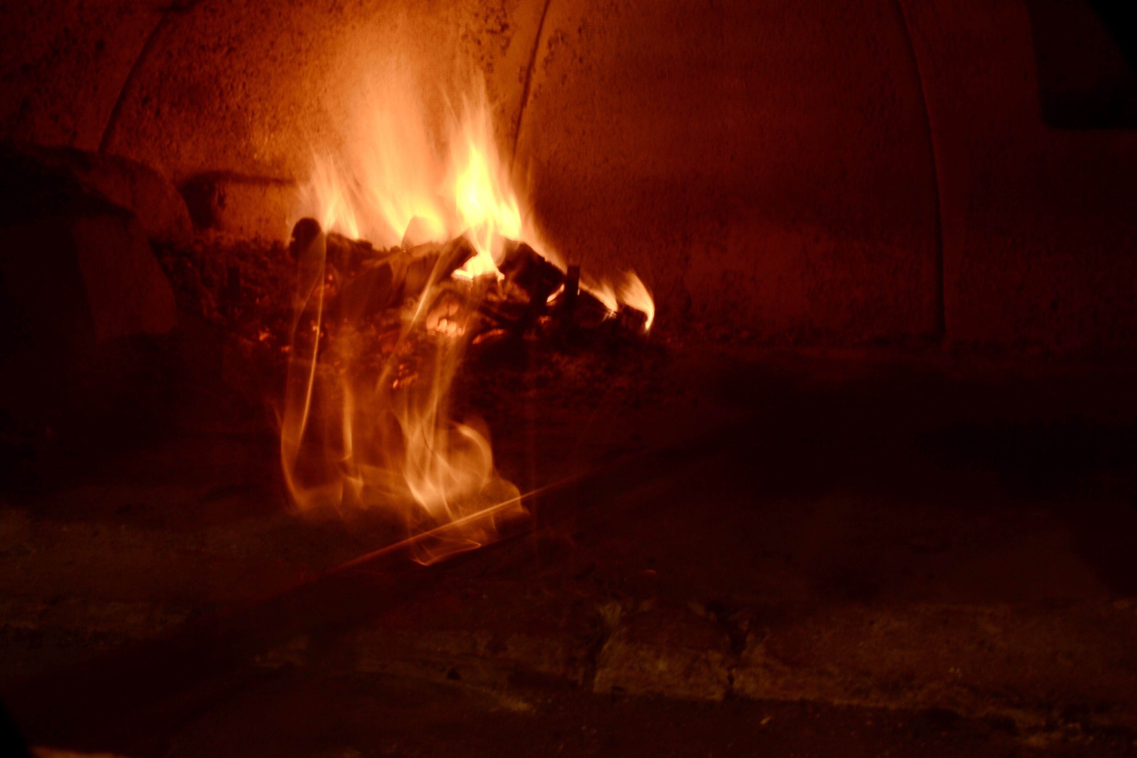 Un fuoco che arde all'interno di una struttura simile a un forno in pietra.