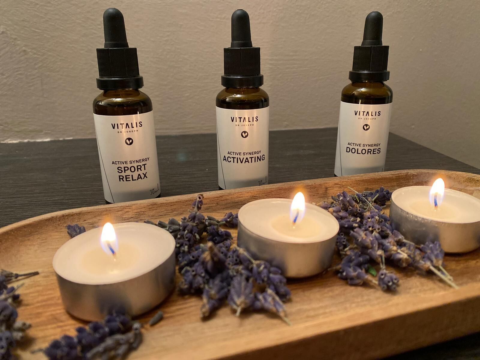 Trois bouteilles de Vitalis Sport Relax sont disposées sur un plateau en bois, accompagnées de bougies allumées et de fleurs de lavande.