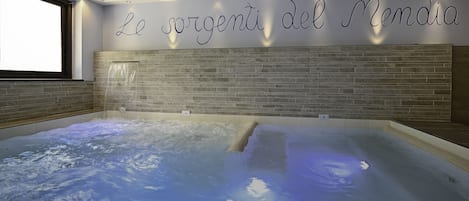 A spa area with a hot tub, a wall with the text "Le sorgenti del Mendaia," and a window on the left.