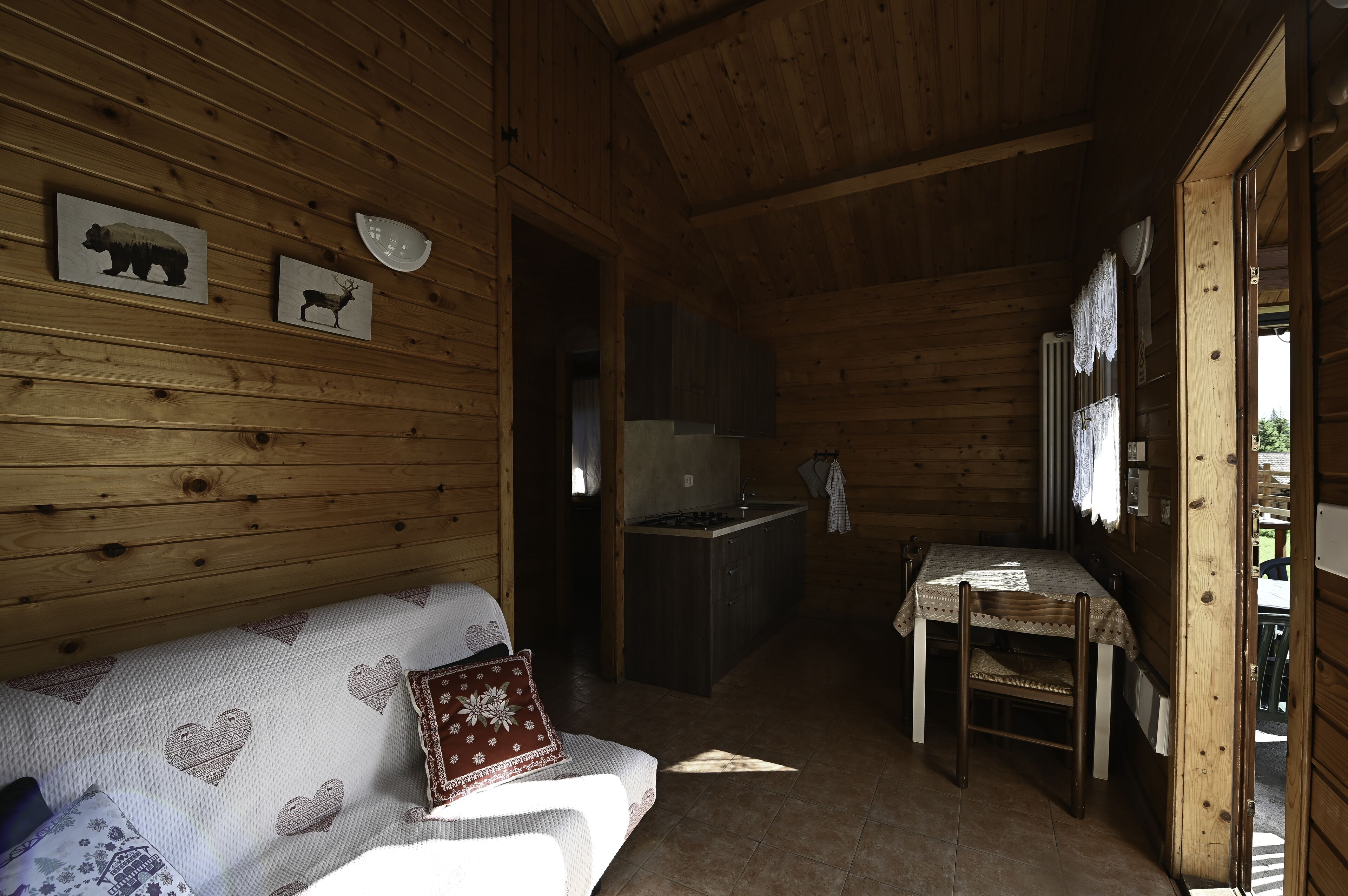 A wooden cabin interior with a sofa, a table, and a kitchen area.