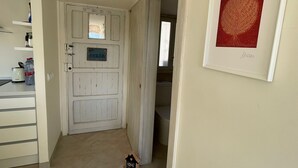 Un pasillo con una puerta blanca, una obra de arte enmarcada en la pared y un pequeño cartel con forma de casa en el suelo.