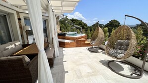 Un patio al aire libre iluminado por el sol con mobiliario de mimbre, un jacuzzi y una pérgola que proporciona sombra.