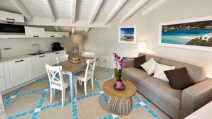 Una cocina moderna con armarios blancos, un comedor con mesa y sillas de madera, un sofá y una mesa baja con una planta.