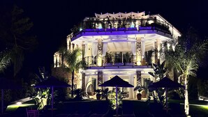 Un edificio de varios pisos con zona de piscina, mobiliario exterior y un balcón bien iluminado.