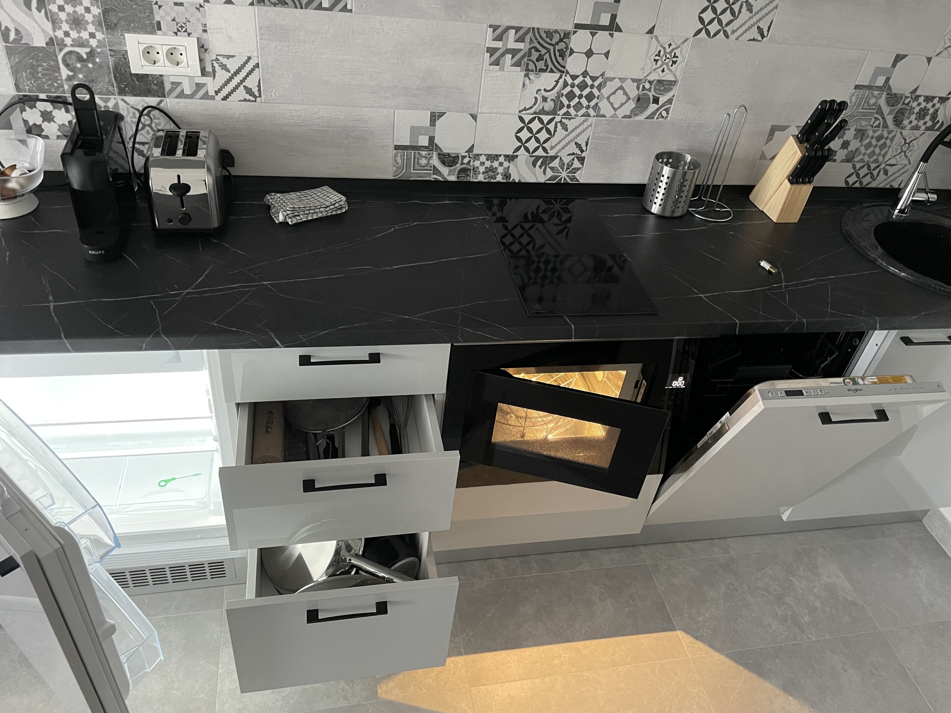 A modern kitchen with a black countertop, white cabinets, and patterned backsplash.