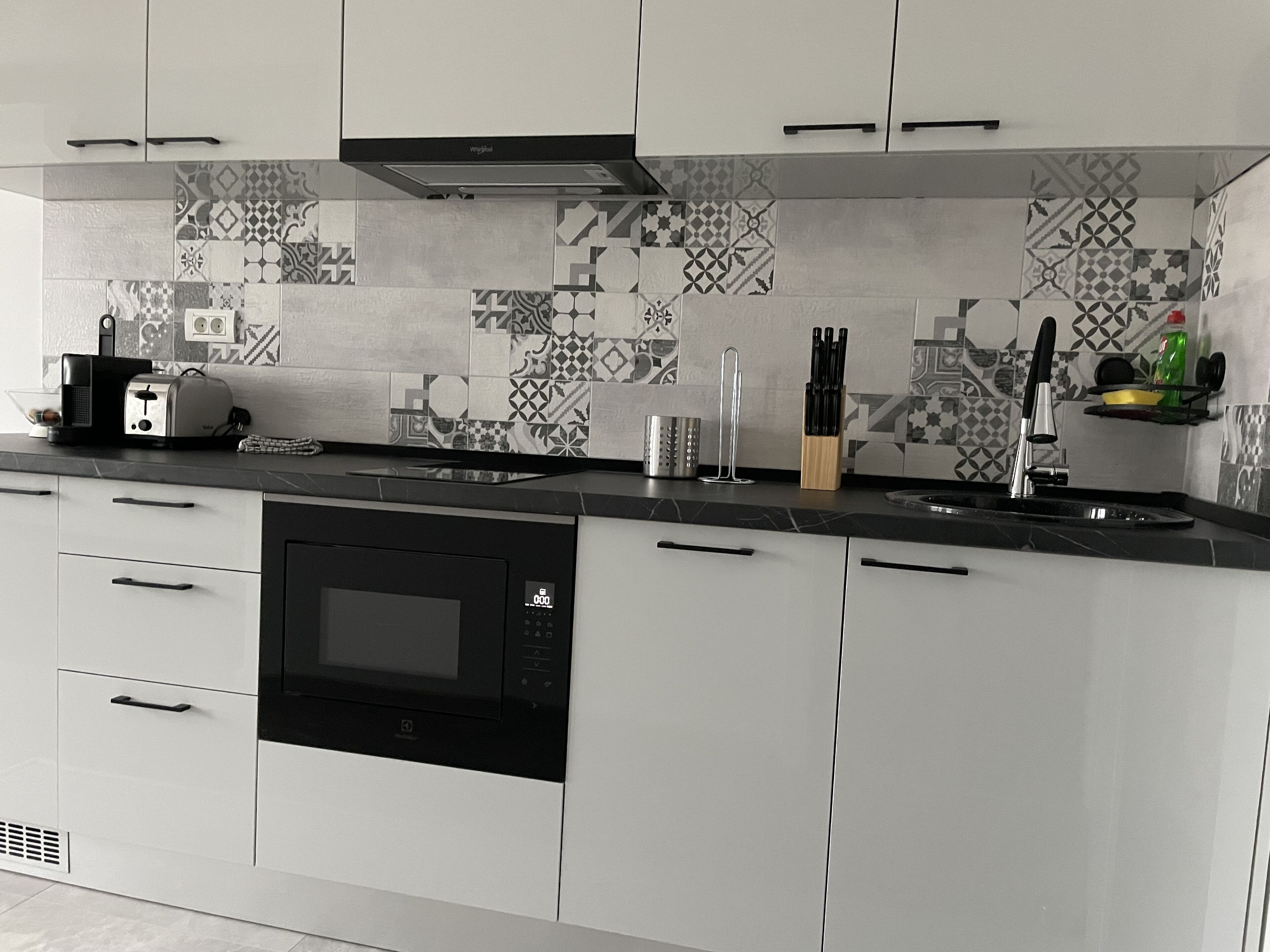 A modern kitchen with white cabinets, a black microwave, and a patterned backsplash.