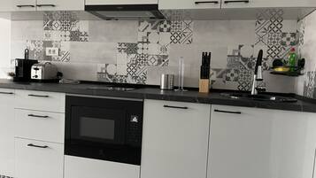 A modern kitchen with white cabinets, a black microwave, and a patterned backsplash.