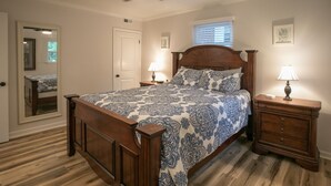 Un dormitorio con una cama de madera, dos mesitas de noche con lámparas, un ventilador de techo y una ventana con persianas.