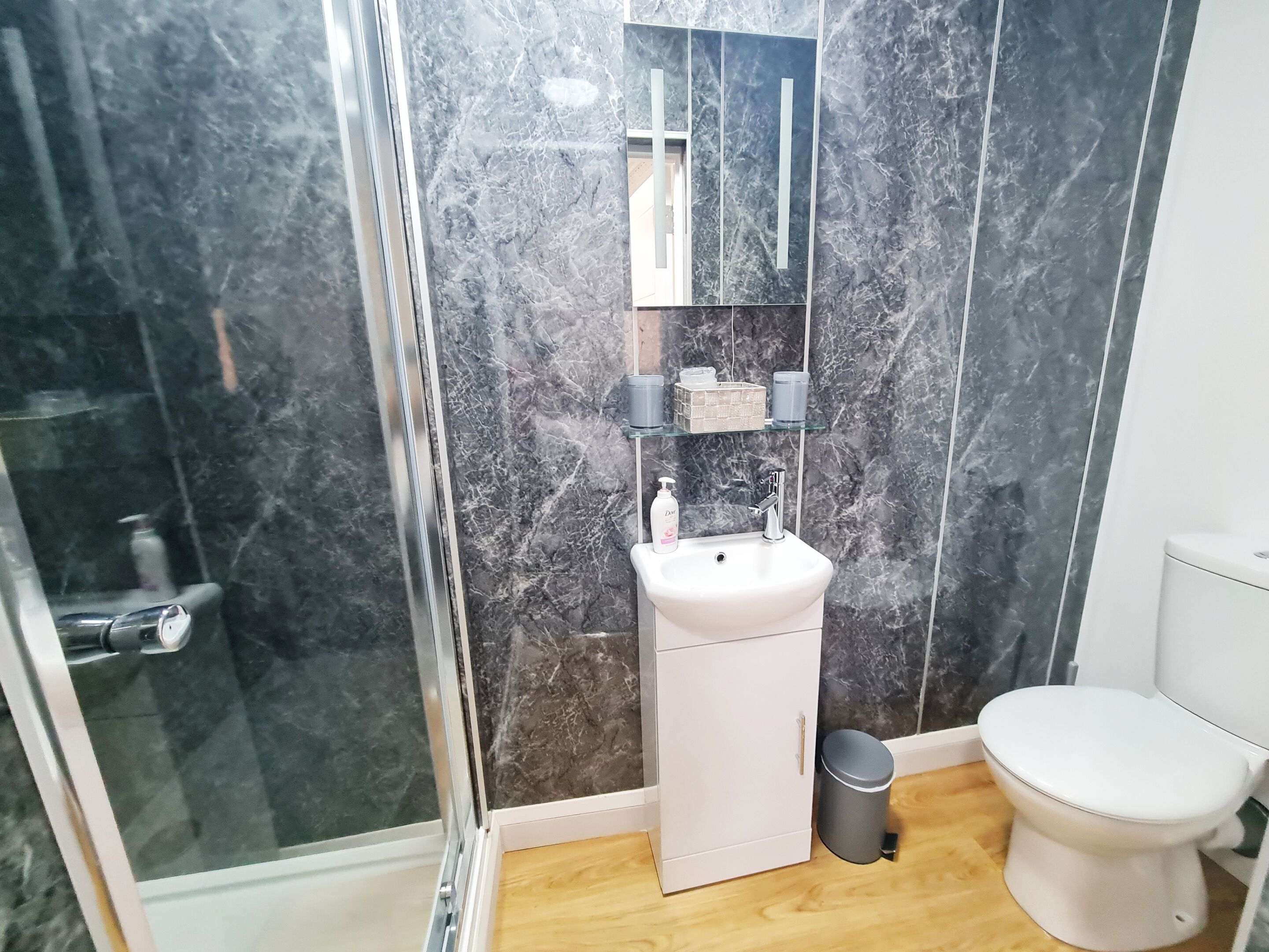 A bathroom with a glass shower enclosure, a white sink, a mirror, and a toilet.