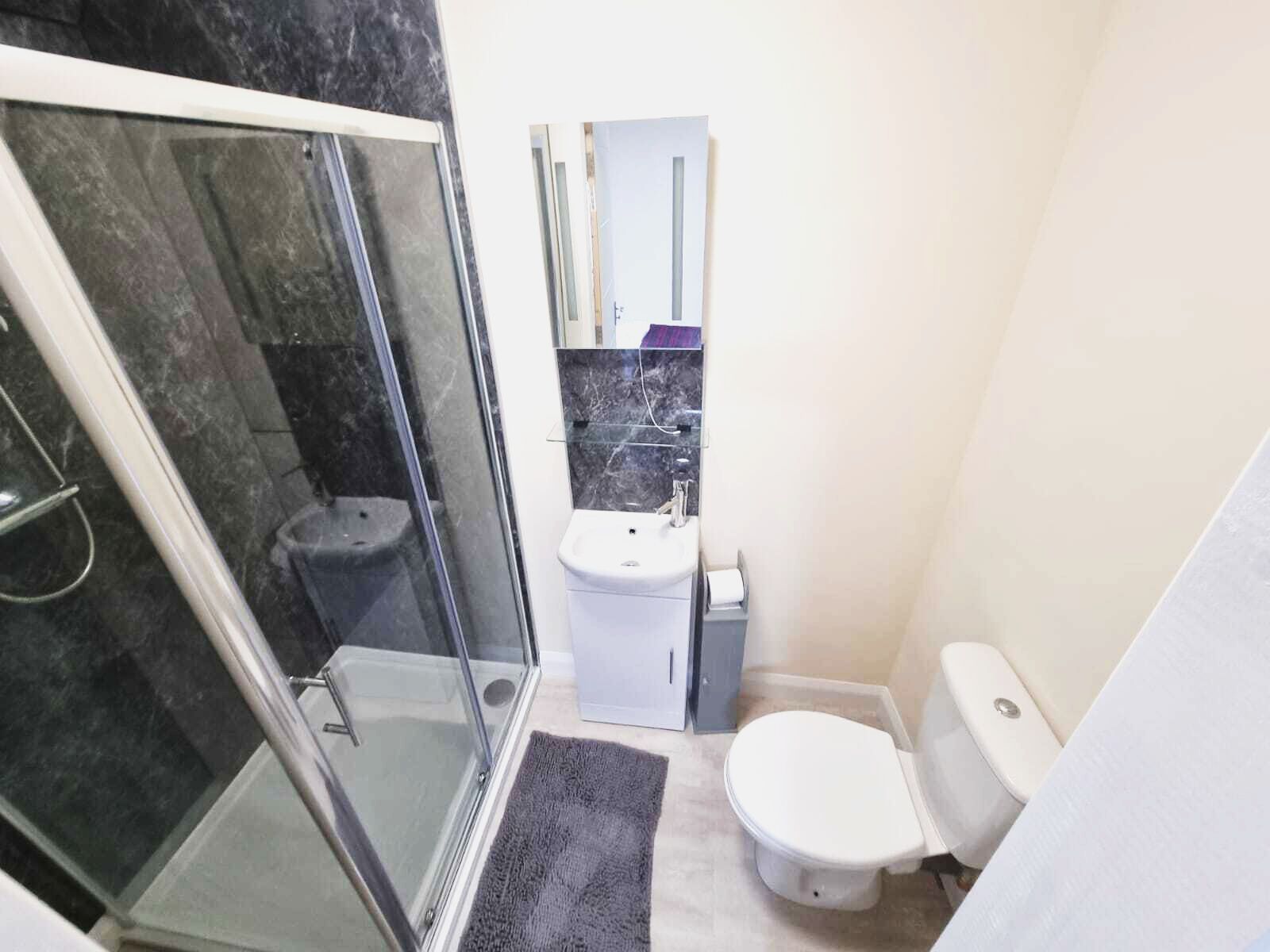 A compact bathroom with a glass shower enclosure, a white toilet, and a sink with a marble countertop.