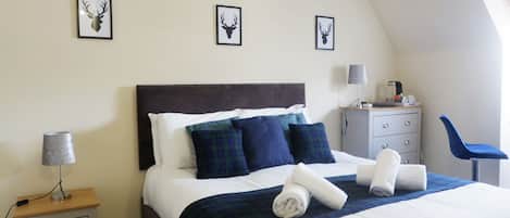 Un dormitorio con una cama, un mesita de noche, un aparador, una silla y tres pares de cornamentas de ciervo enmarcadas en la pared.