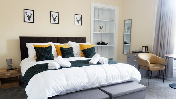 A neatly made bed with a dark headboard, multiple pillows, and a bedside table with a lamp. - Jacobite house (Inverness)