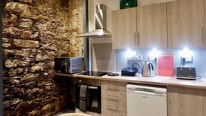 A kitchen with a stone wall, wooden cabinets, a microwave, a toaster, and a dishwasher. - Jacobite house (Inverness)