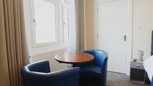 A hotel room with a round wooden table, two blue chairs, a white door, and a window with curtains. - Jacobite house (Inverness)