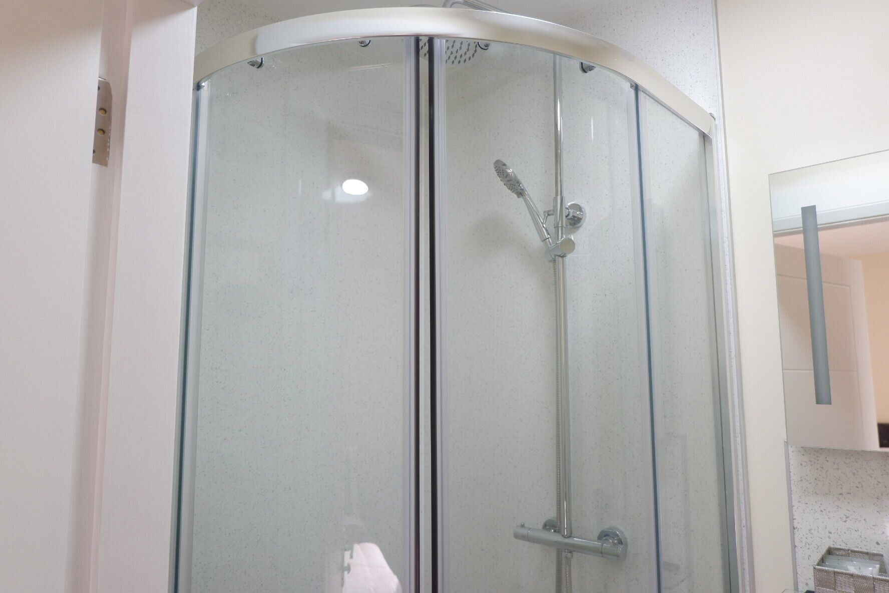 Une douche fermée par des parois en verre, dotée d’un pommeau de douche à main et d’un panneau de commande fixé au mur.
